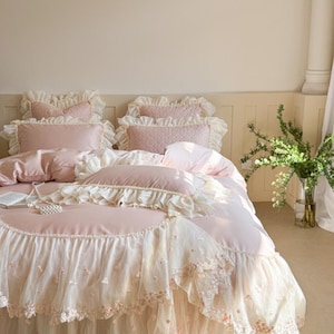 May include: A pink bedspread and pillow set with frilled edges and a delicate floral design. The bedding has a soft, romantic aesthetic, with a layered look and a touch of vintage charm. The set includes multiple pillows and a bed skirt.