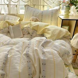 May include: A bed with a white metal headboard and a bedding set. The bedding features a white and yellow striped pattern with small dog illustrations. Yellow pillows and a book are also visible.