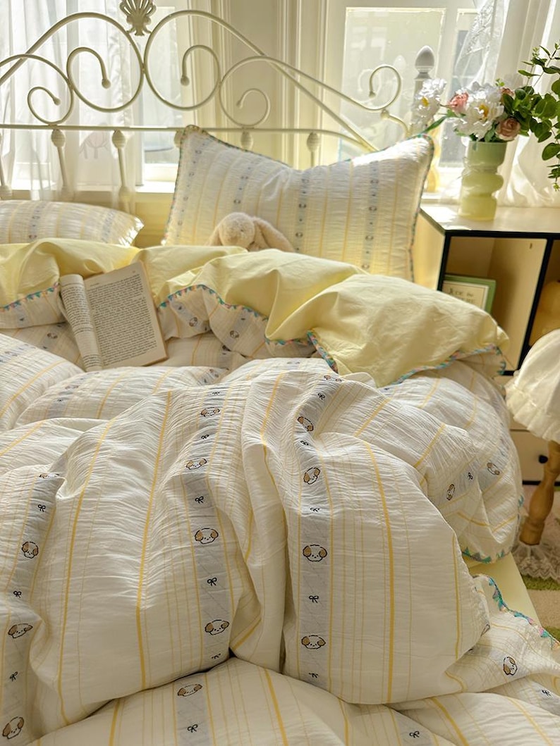 May include: A bed with a white metal headboard and a bedding set. The bedding features a white and yellow striped pattern with small dog illustrations. Yellow pillows and a book are also visible.