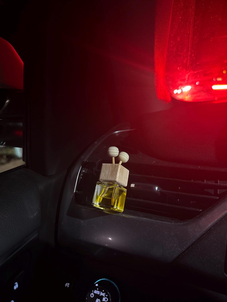 Pu&ograve; includere: Un piccolo profumatore per auto in vetro trasparente con una parte superiore in legno e due accenti sferici. Il liquido all'interno &egrave; giallo. Il profumatore &egrave; posto su una bocchetta di ventilazione del cruscotto dell'auto.