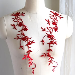 May include: Two red floral appliques with a vine design. The appliques are made of fabric and have a delicate, feminine look.