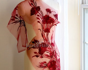 May include: Red floral embroidered lace fabric on a white dress form. The lace is sheer and has a delicate floral design. The fabric is perfect for adding a touch of elegance to any project.