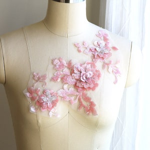 May include: A pink floral applique with sequins and beads on a white dress form.