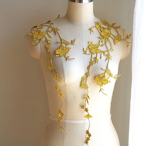May include: A pair of gold floral appliques with delicate leaves and flowers. The appliques are displayed on a white dress form.