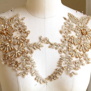 Może przedstawiać: Złota aplikacja kwiatowa z koralików i cekinów z delikatnym wzorem liści. Ta ozdoba idealnie nadaje się do dodania blasku i elegancji ubraniom, akcesoriom lub projektom dekoracyjnym.