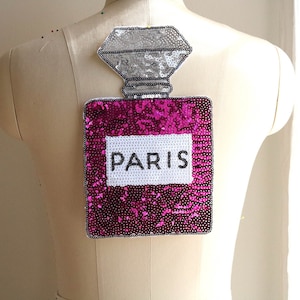 May include: A pink and silver sequined iron-on patch shaped like a perfume bottle with the word "PARIS" on the label.