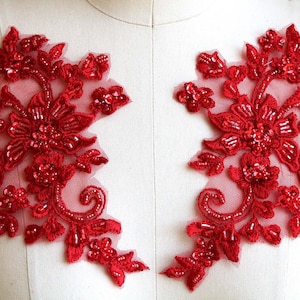 Könnte beinhalten: Zwei rote, perlenbesetzte florale Spitzenapplikationen mit einem zarten Blumenmuster und Pailletten. Die Applikationen sind perfekt, um jedem Projekt einen Hauch von Eleganz zu verleihen.