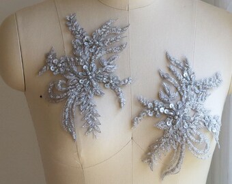 May include: Two silver sequined and beaded floral appliques. The appliques are on a white mannequin form.