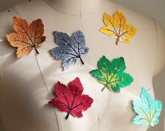 Può includere: Sei toppe di foglie d'acero in feltro ricamate in vari colori, tra cui arancione, grigio, verde, rosso e blu, esposte su un manichino bianco.
