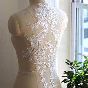 May include: White lace applique with a floral design. The lace is delicate and intricate, with a variety of floral motifs. It is perfect for adding a touch of elegance to any garment.