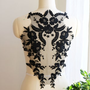 Peut inclure: Applique en dentelle florale noire avec un motif délicat. La dentelle est sur un fond de tulle transparent et est parfaite pour ajouter une touche d'élégance à n'importe quel vêtement.