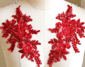 May include: Two red beaded floral appliques with sequins and leaves. The appliques are on a white background.