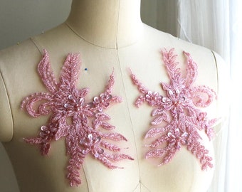 Puede incluir: Dos apliques de encaje floral rosa con lentejuelas y cuentas. Los apliques están en un maniquí blanco.