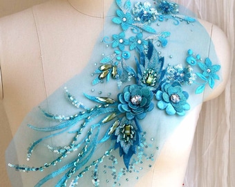 May include: A turquoise blue floral applique with sequins and beads on a sheer fabric. The applique is on a white dress form.