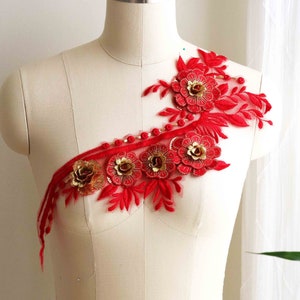 Puede incluir: Aplique de encaje floral rojo y dorado con detalles de cuentas. El aplique presenta un delicado diseño floral con tres flores grandes y hojas más pequeñas. El aplique es perfecto para agregar un toque de elegancia a cualquier prenda.