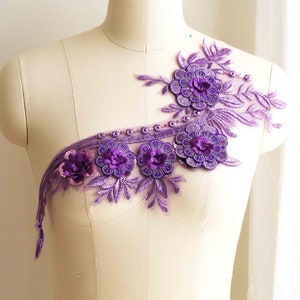 May include: Purple floral lace applique with beaded accents. The applique features several flower designs with a delicate, intricate pattern.
