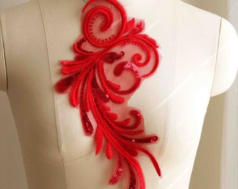 May include: Red sequined lace applique with a floral design. The applique is on a white mannequin.