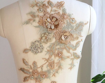 May include: A delicate floral applique with beige and green embroidery and pearl accents. The applique is perfect for adding a touch of elegance to clothing or accessories.