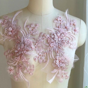 May include: Pale pink floral lace applique with embroidered flowers and beaded accents. The delicate design features multiple floral clusters and trailing stems, perfect for embellishing garments or crafts.