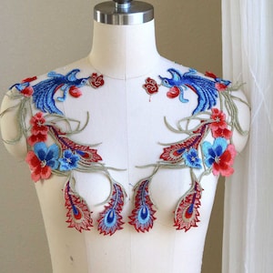 May include: A pair of blue and red embroidered appliques featuring peacocks and flowers. The appliques are on a white background and are perfect for adding a touch of elegance to any project.