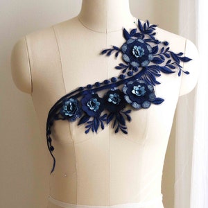 Puede incluir: Aplique floral azul marino con lentejuelas y abalorios. El aplique presenta un grupo de flores con hojas y tallos. El aplique está sobre un fondo blanco.