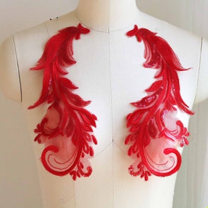 May include: Two red lace appliques with a floral design. The appliques are made of a sheer fabric with a red embroidered pattern.