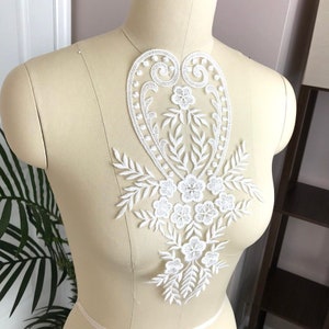 May include: White lace applique with a floral design and a heart shape. The applique is perfect for adding a touch of elegance to any garment.