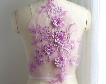 May include: A lavender floral applique with 3D flowers, leaves, and sparkling rhinestones. The applique is made of delicate lace and is displayed on a mannequin. This decorative applique is perfect for embellishing garments.