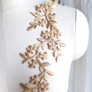 May include: A delicate gold floral applique with a vine design. The applique features small flowers and leaves, perfect for adding a touch of elegance to clothing or crafts.
