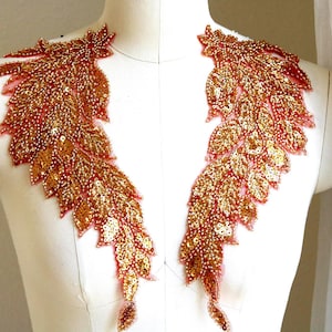 May include: A pair of gold and coral colored beaded applique embellishments, each shaped like a stylized leaf, with a delicate, sheer fabric backing.