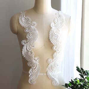 May include: Two white lace appliques with a feather design. The appliques are displayed on a dress form.