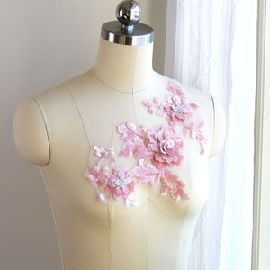 May include: A pink floral applique with sequins and pearls on a white dress form.