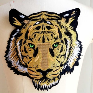 May include: Embroidered iron-on patch of a tiger's face with gold and black fur and green eyes.