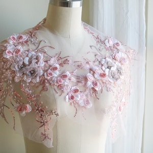 以下が含まれることがあります： 透き通るメッシュ生地に、ピンクと白の繊細な花柄のアップリケが施されています。キラキラ光るスパンコールとビーズがアクセントになっています。このアップリケは、洋服やアクセサリー、インテリアにエレガントなアクセントを加えるのに最適です。