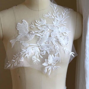以下が含まれることがあります： ウェディングドレスやその他の衣服にエレガントなタッチを加えるのに最適な、鳥と蝶の白いレースアップリケです。