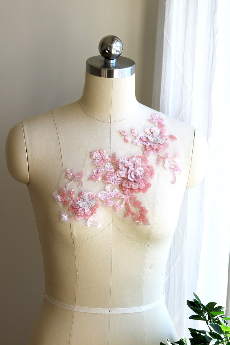 May include: A pink floral applique with sequins and beads on a white dress form.