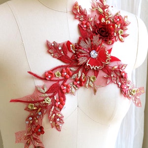 May include: Red and gold floral applique with sequins and beads. The applique features a large red flower with a crystal center and smaller red flowers and leaves.