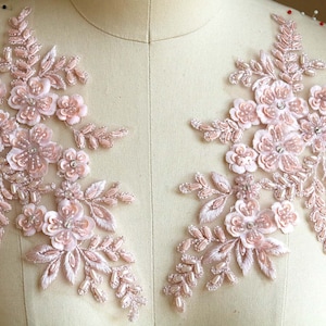 May include: Two delicate pink floral appliques with pearl and rhinestone embellishments. These appliques are perfect for adding a touch of elegance to wedding dresses, bridal accessories, or other special occasion garments.
