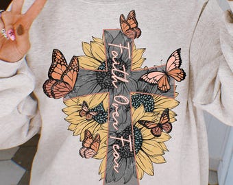 May include: Light gray sweatshirt featuring a cross design made of sunflowers and butterflies. The cross has the words "Faith Over Fear" printed on it. The butterflies are in shades of orange and pink.