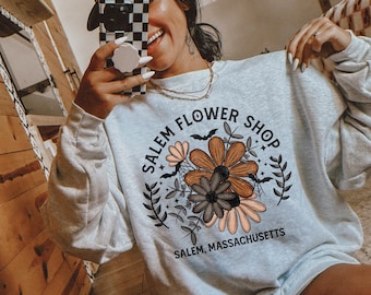 Może przedstawiać: Jasno błękitna bluza z nadrukiem graficznym z kompozycją kwiatową i tekstem "Salem Flower Shop" oraz "Salem, Massachusetts".