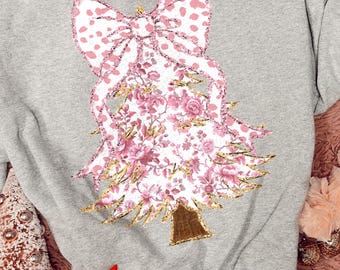 May include: A heather grey crewneck sweatshirt featuring a large graphic of a Christmas tree made of pink floral patterns and a pink leopard print bow at the top. The tree design includes gold glitter accents along the branches and a brown trunk.
