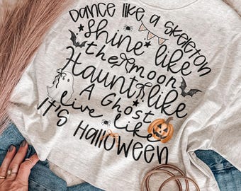 May include: A light gray t-shirt featuring black text that reads: Dance like a skeleton, Shine like the moon, Haunt like a ghost, Live like it's Halloween. The design includes small illustrations of a bat, a spider, a pumpkin, and bunting.