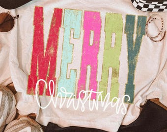 May include: A white t-shirt featuring the word MERRY in large, distressed, multi-colored block letters of red, light blue, pink, lime green, and dark teal, with the word Christmas written below in a white, cursive, handwritten-style font.