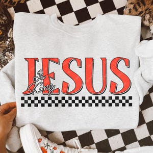 May include: A gray sweatshirt with the words "JESUS is King" in red letters with a black and white checkered pattern below the text.