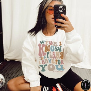 May include: White sweatshirt with a colorful graphic design that reads "For I know the plans I have for you" with a butterfly on each side and the text "Jeremiah 29:11" at the bottom.