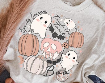 May include: A light gray crewneck sweatshirt featuring a graphic print with ghosts, pumpkins, bats, a skull, and a disco ball. The text reads Spooky Season, Trick Or Treat, and Boo in black script. The design includes soft pink and orange accents.
