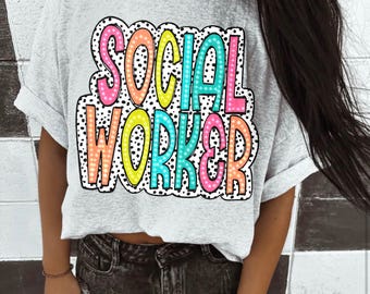 Op de afbeelding: Een lichtgrijs t-shirt met korte mouwen en de tekst SOCIAL WORKER in een veelkleurig, gestippeld lettertype. De letters zijn gevuld met roze, oranje, geel en turquoise, zwart omlijnd op een witte achtergrond met zwarte stippen.