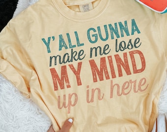 Op de afbeelding: Een geel T-shirt met de tekst "Y'all Gunna make me lose MY MIND up in here" in een vintage lettertype met rode, blauwe en groene kleuren.