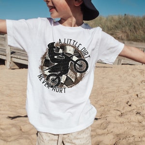 May include: White t-shirt with a black and white graphic of a dirt bike rider with the text "A Little Dirt Never Hurt".