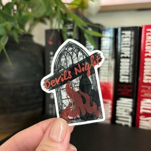 Puede incluir: Una pegatina en blanco y negro con un diseño de ventana gótica. La ventana está en llamas y el texto "Devil's Night" está escrito en la parte superior.